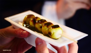 Na druhé straně světa se naši tanečníci zakusují do japonského „aburi-mochi,“ grilovaného rýžového zákusku napichovaného na špejli – tisíce let staré kjótské cukrovinky.